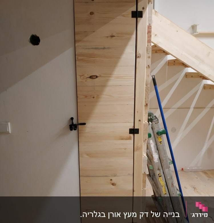 דלת עץ עם צירים ובריח ליד סולם ומטאטא